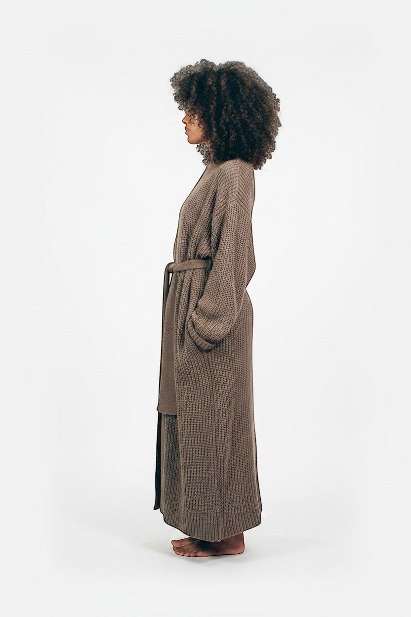 AMI CHÉRIE DESIGN STUDIO taupe longline knit robe with belt and pockets, worn by a woman with curly hair.